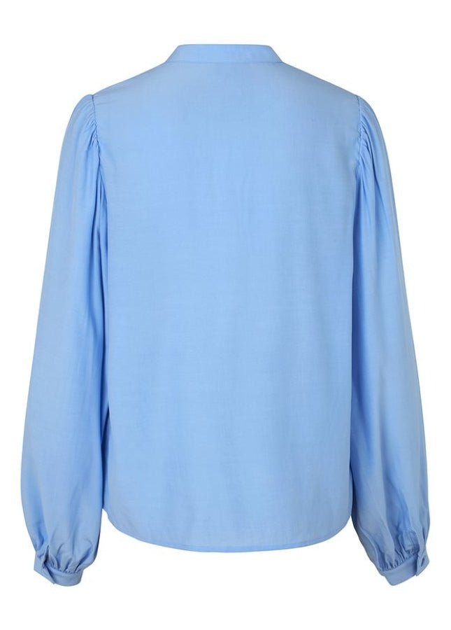 Mooie lichtblauwe blouse Keli van het merk mbyM. De blouse met mandarijnkraag en plooitjes aan de voorkant heeft lange mouwen met manchetten. De blouse heeft een ronde hals, een halve knoopsluiting aan de voorkant en een relaxte pasvorm. Shop de nieuwe collectie dames blouses, lichtblauwe blouses, mbyM blouses online.