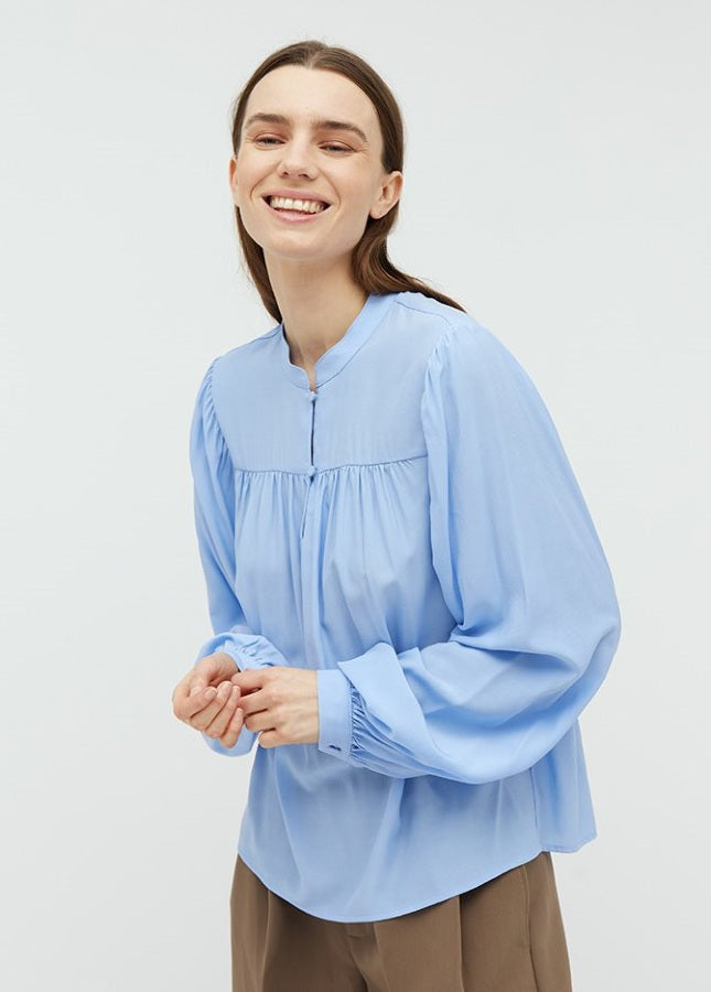 Mooie lichtblauwe blouse Keli van het merk mbyM. De blouse met mandarijnkraag en plooitjes aan de voorkant heeft lange mouwen met manchetten. De blouse heeft een ronde hals, een halve knoopsluiting aan de voorkant en een relaxte pasvorm. Shop de nieuwe collectie dames blouses, lichtblauwe blouses, mbyM blouses online.