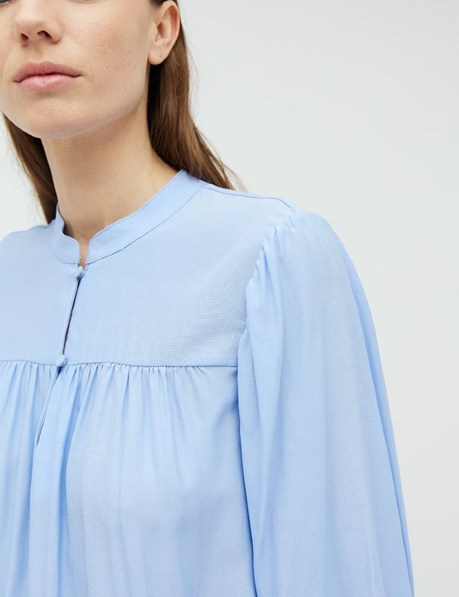 Mooie lichtblauwe blouse Keli van het merk mbyM. De blouse met mandarijnkraag en plooitjes aan de voorkant heeft lange mouwen met manchetten. De blouse heeft een ronde hals, een halve knoopsluiting aan de voorkant en een relaxte pasvorm. Shop de nieuwe collectie dames blouses, lichtblauwe blouses, mbyM blouses online.
